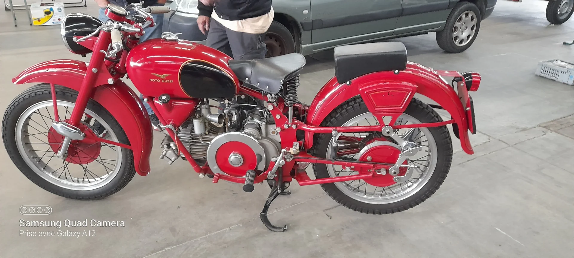 Une moto Moto Guzzi rouge vintage au design élégant, avec une selle noire et des détails chromés, est garée à l'intérieur.